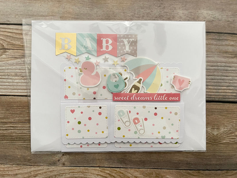 Baby-themed card with illustrations and text on a wooden surface