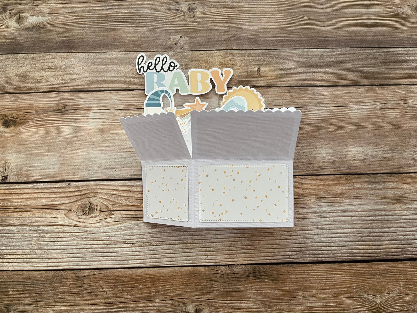 Open baby card with 'hello baby' text and illustrations on a wooden surface