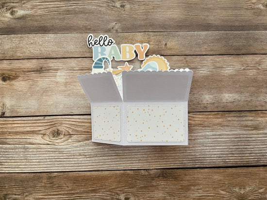Open baby card with 'hello baby' text and illustrations on a wooden surface