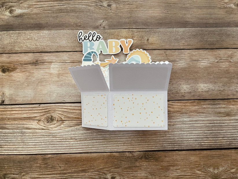 Open baby card with 'hello baby' text and illustrations on a wooden surface