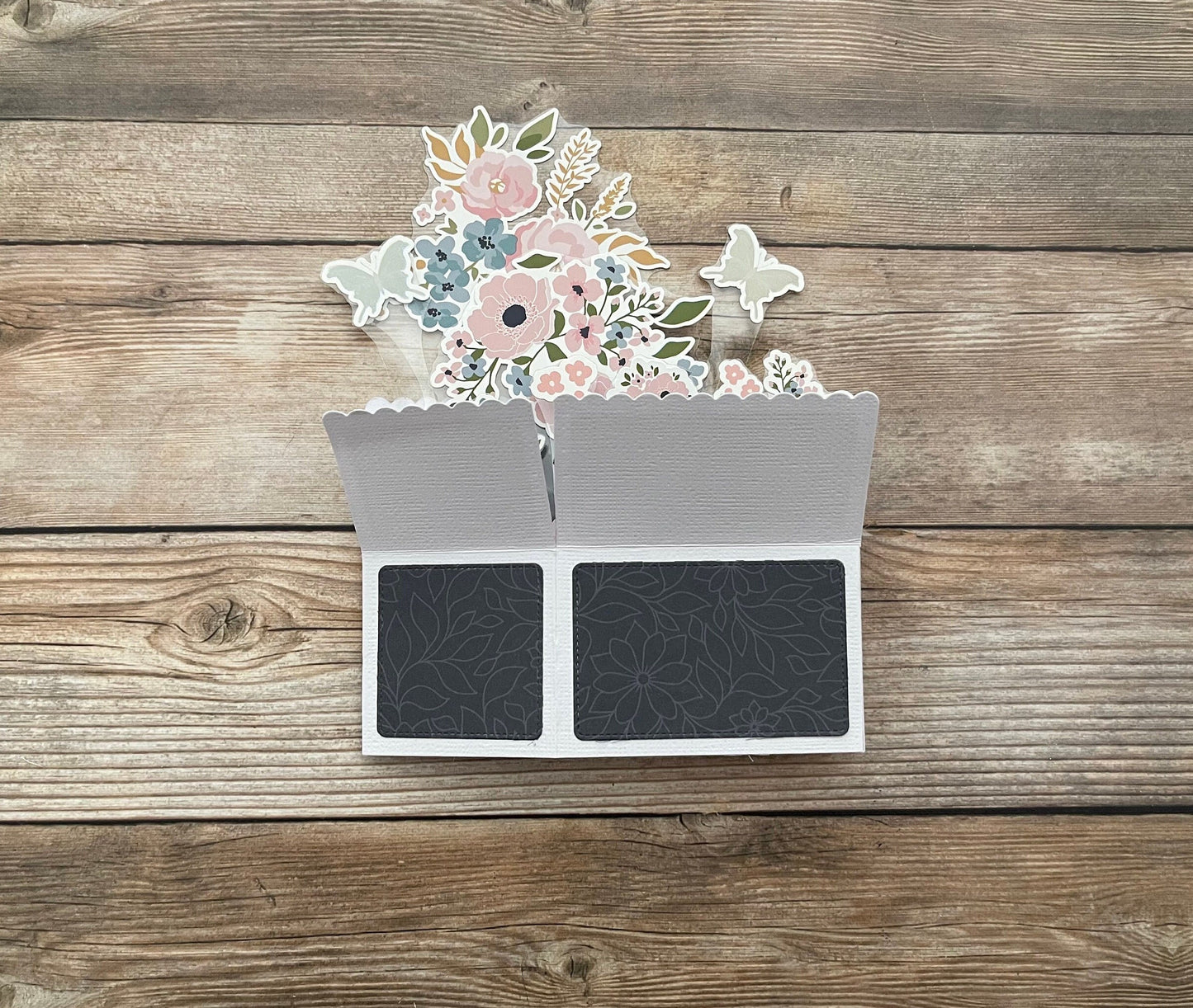 Floral design on a card with two black cardstocks on a wooden surface