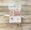 Open pop-up card with baby's first birthday themed designs on a wooden surface