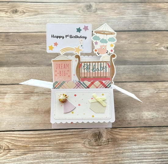 Open pop-up card with baby's first birthday themed designs on a wooden surface