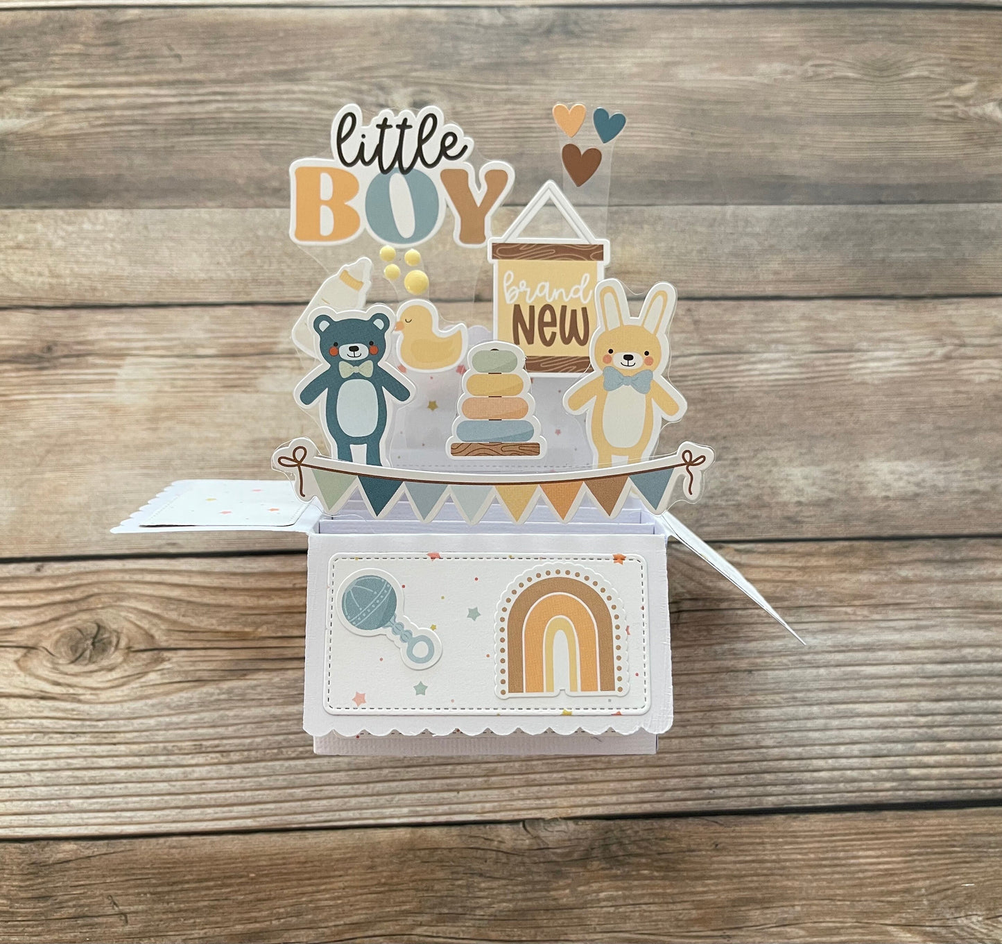 Baby-themed card with illustrations of a teddy bear, baby shower elements, and text on a wooden background.