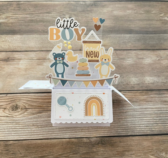Baby-themed card with illustrations of a teddy bear, baby shower elements, and text on a wooden background.