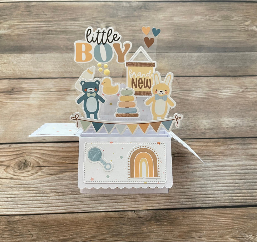 Baby-themed card with illustrations of a teddy bear, baby shower elements, and text on a wooden background.