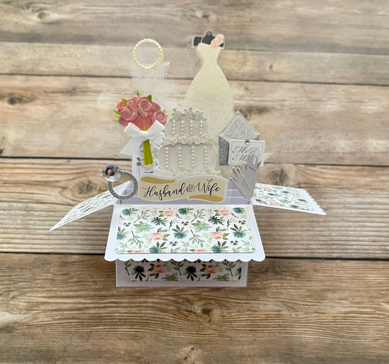 Pop-up wedding card with bride, cake, ring, and flowers on a wooden background