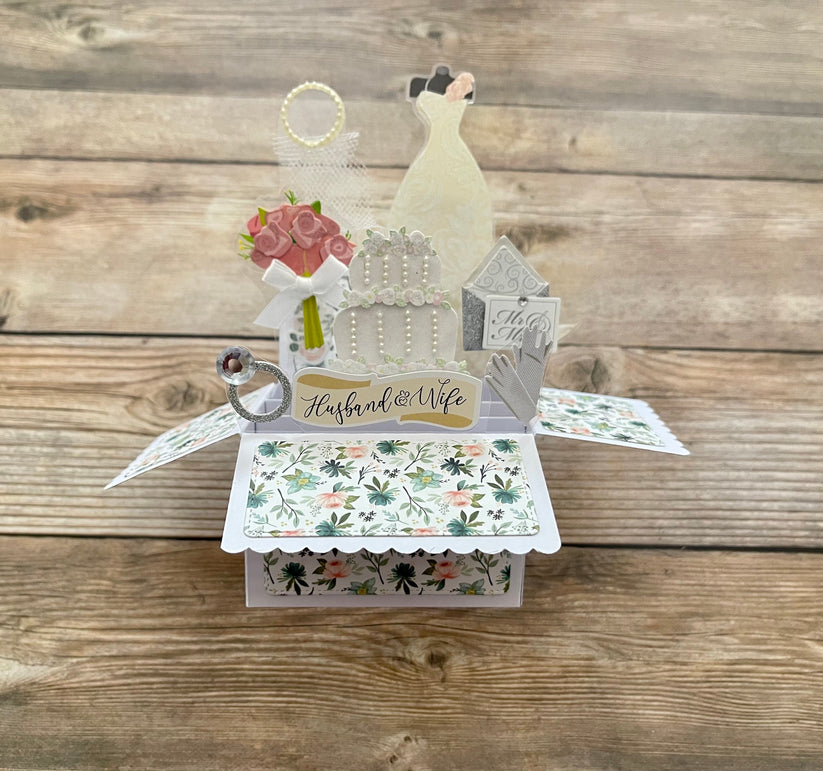 Pop-up wedding card with bride, cake, ring, and flowers on a wooden background