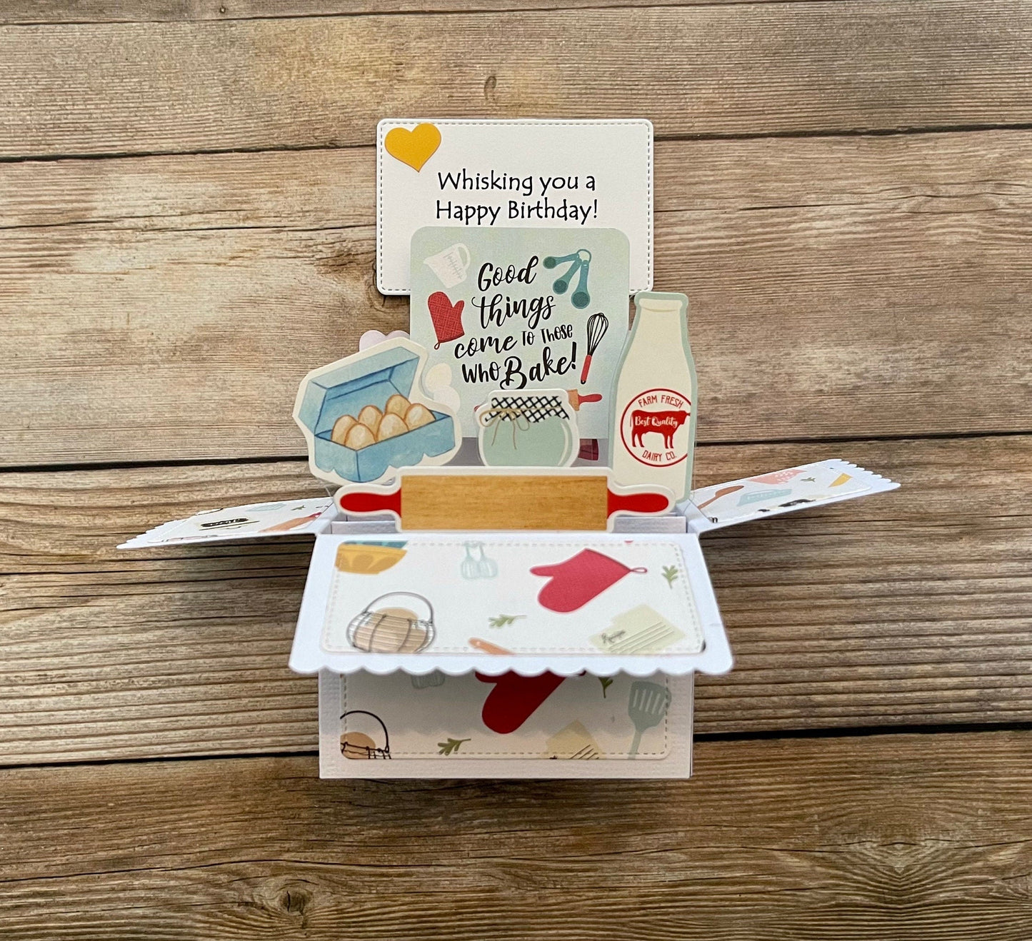 Open pop-up card with kitchen-themed illustrations on a wooden surface