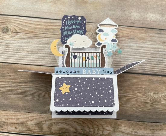 Baby shower card with crib, stars, and moon design on a wooden surface