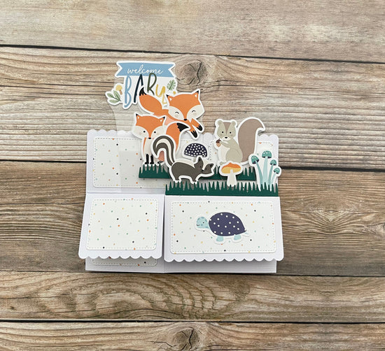 3D box pop-up baby card with fox and squirrel design on a wooden surface