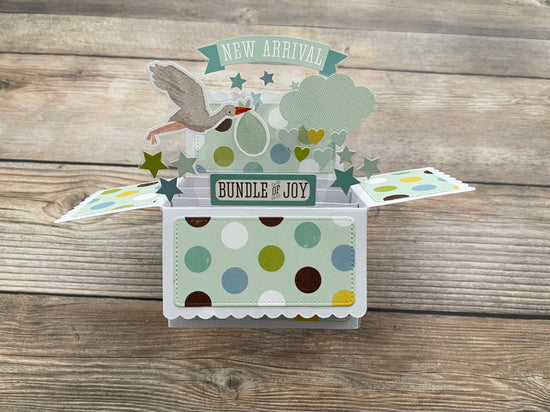 Pop-up baby card with 'New Arrival' and 'Bundle of Joy' text on a wooden surface