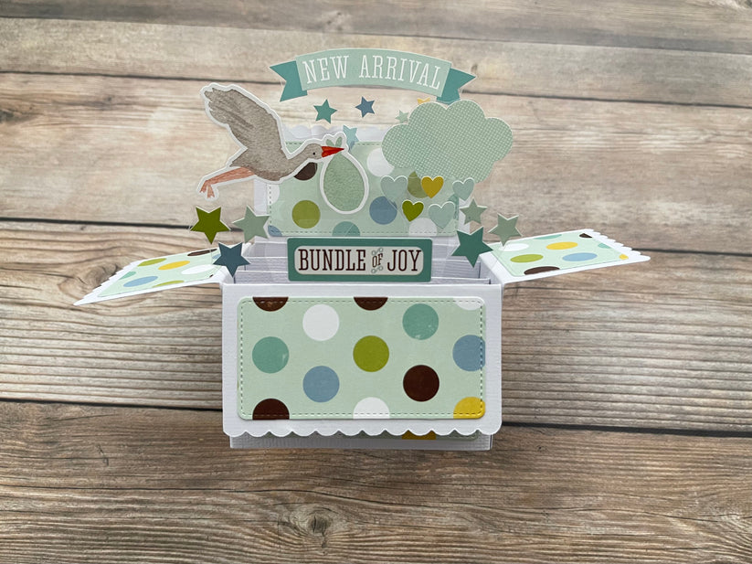 Pop-up baby card with 'New Arrival' and 'Bundle of Joy' text on a wooden surface