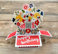 Pop-up birthday card with floral design and 'happy birthday' text on a wooden surface