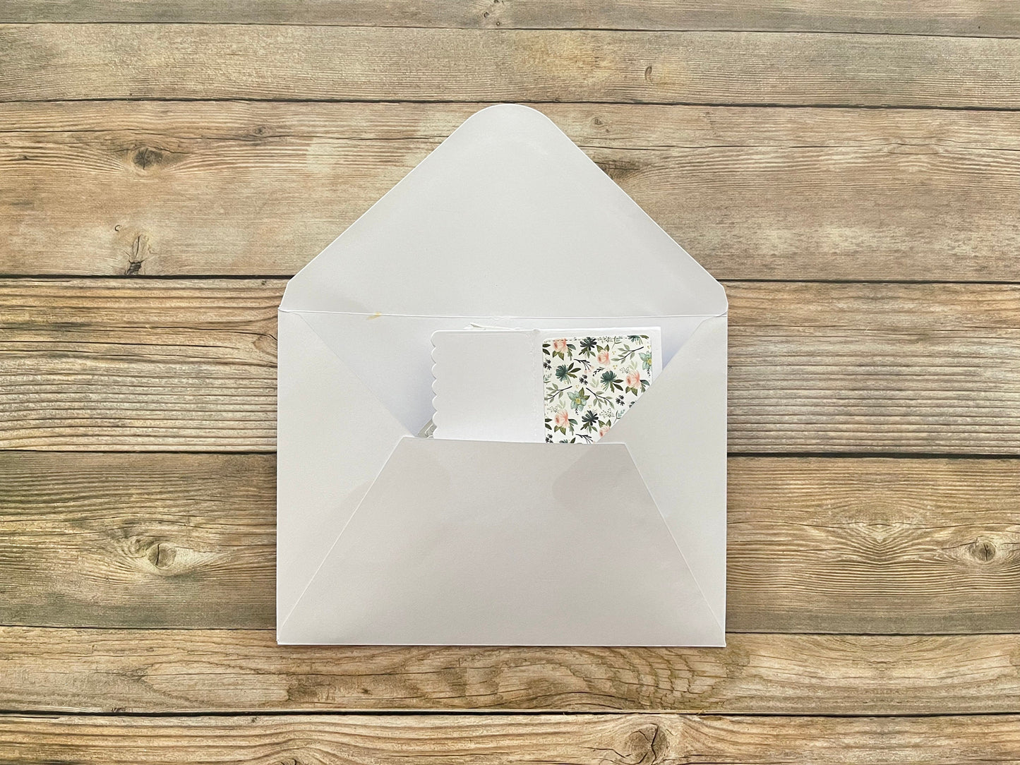 White envelope with a floral card on a wooden surface