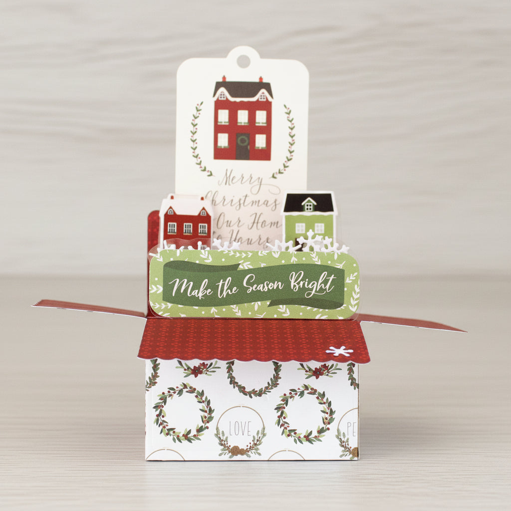 Christmas-themed box style pop-up card with decorative houses and text on a wooden surface.