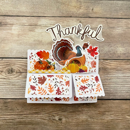 Thanksgiving-themed card with turkey, pumpkins, and fall leaves on a wooden background