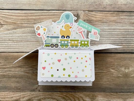 Colorful baby-themed pop-up card with animals on a wooden surface