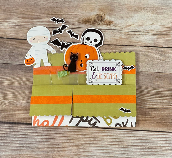 Halloween-themed decorative pop-up card with ghost, pumpkin, and cat on a wooden background