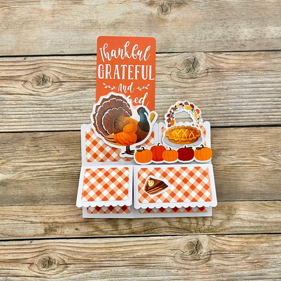 Thanksgiving-themed card with illustrations of a turkey, pie, and pumpkins on a wooden background.