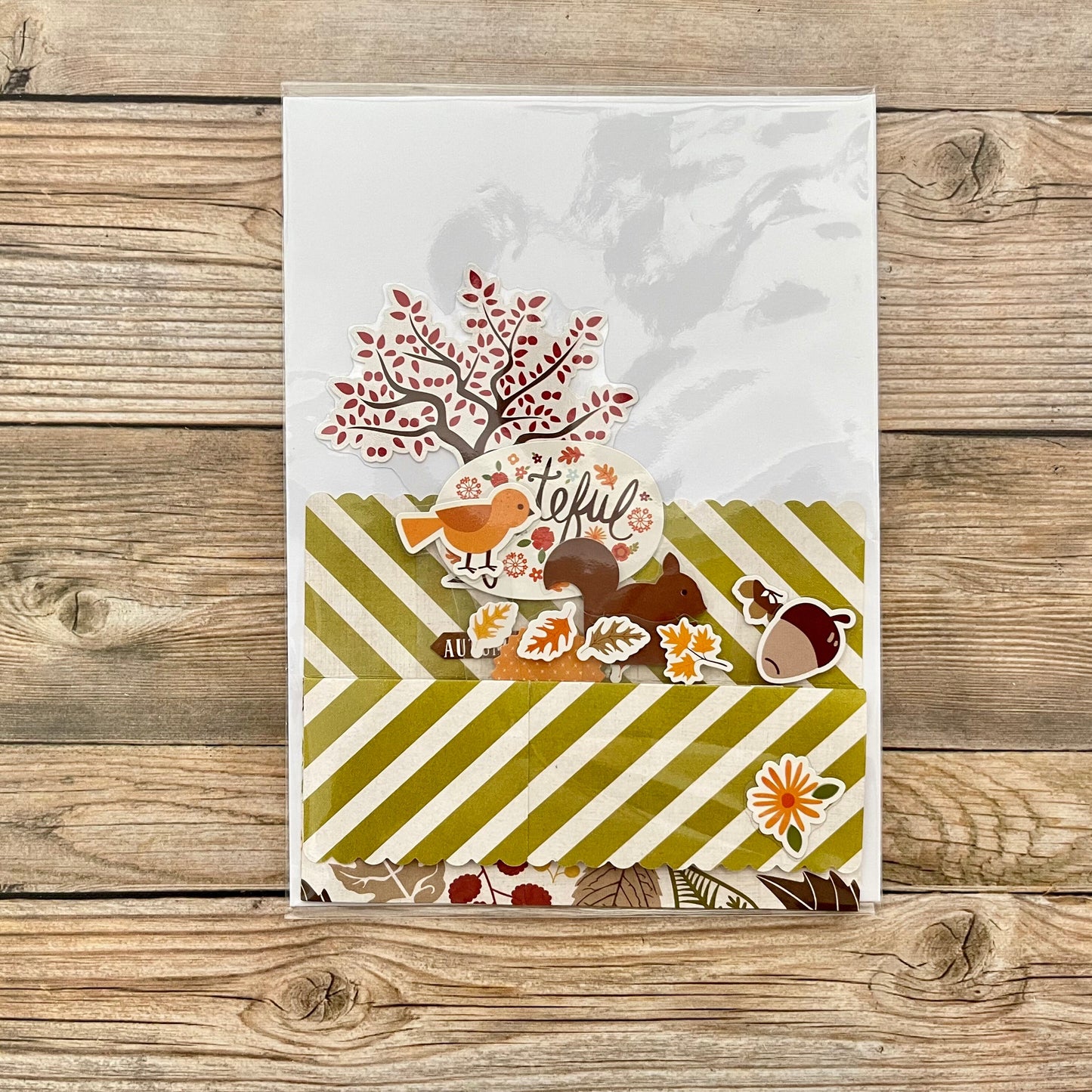 Autumn-themed card with trees, birds, and acorns on a wooden surface