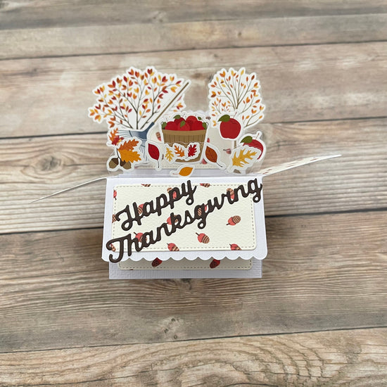 Thanksgiving-themed card with fall decorations on a wooden surface
