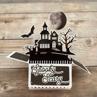 Halloween-themed pop-up box with a haunted house design on a wooden surface.