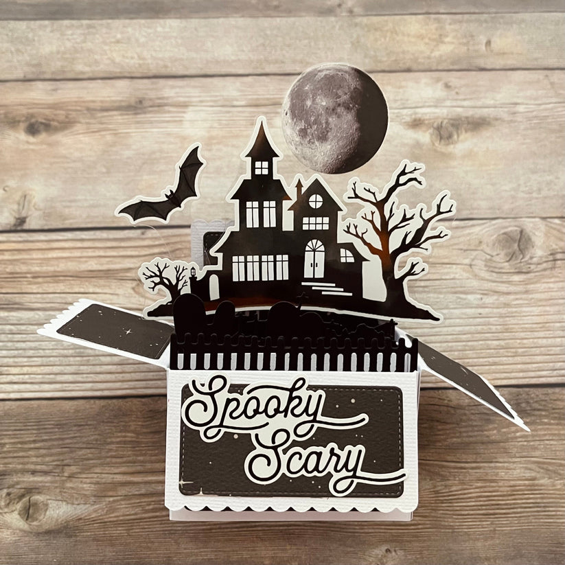 Halloween-themed pop-up box with a haunted house design on a wooden surface.