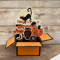 Halloween-themed pop-up box with cat, owl, and pumpkin designs on a wooden background