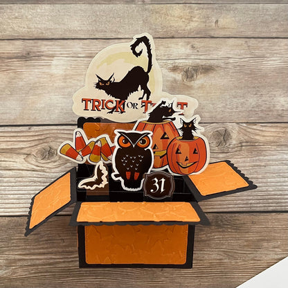 Halloween-themed pop-up box with cat, owl, and pumpkin designs on a wooden background