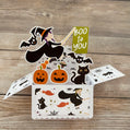 Halloween-themed pop-up card with witch, pumpkins, and cats on a wooden surface