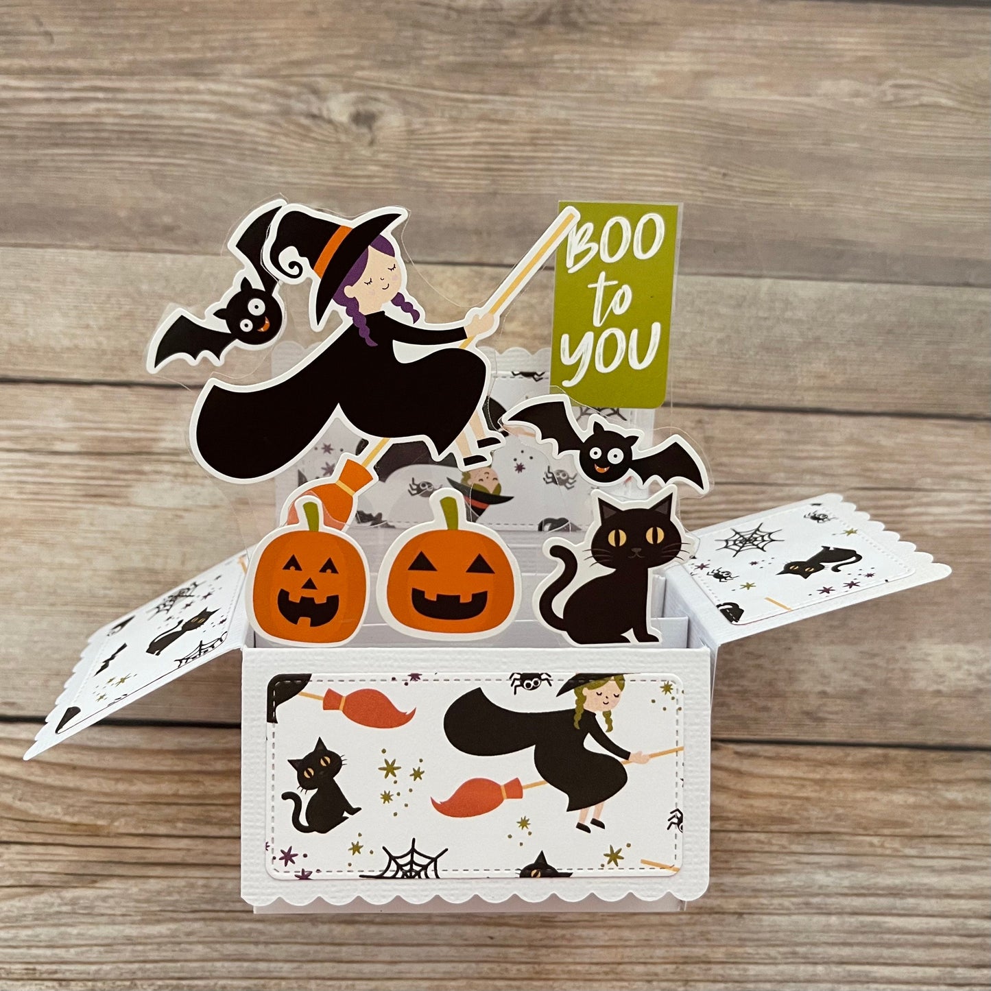 Halloween-themed pop-up card with witch, pumpkins, and cats on a wooden surface