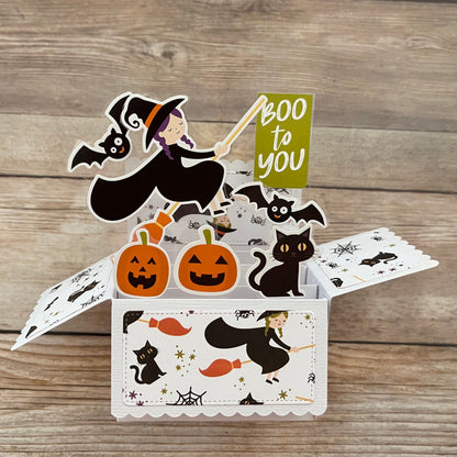 Halloween-themed pop-up card with witch, pumpkins, and cats on a wooden surface