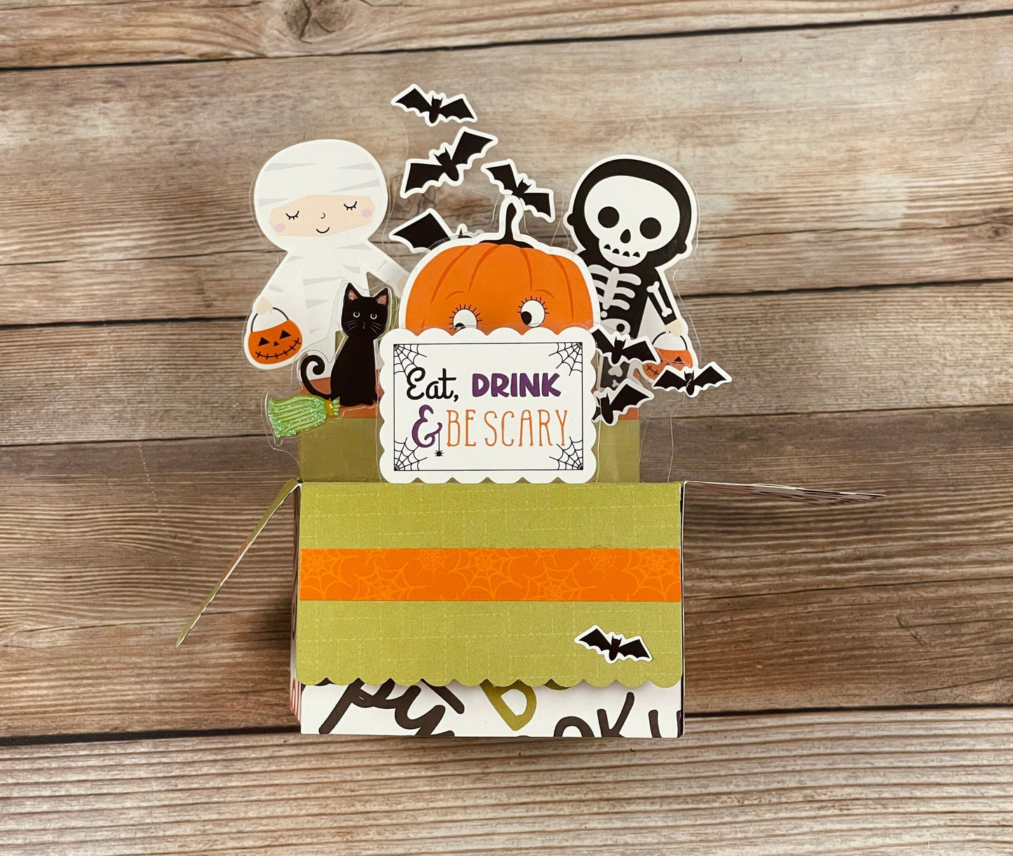 Halloween-themed decorative box pop-up card with ghost, cat, pumpkin, and skeleton on a wooden background
