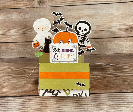 Halloween-themed decorative box pop-up card with ghost, cat, pumpkin, and skeleton on a wooden background
