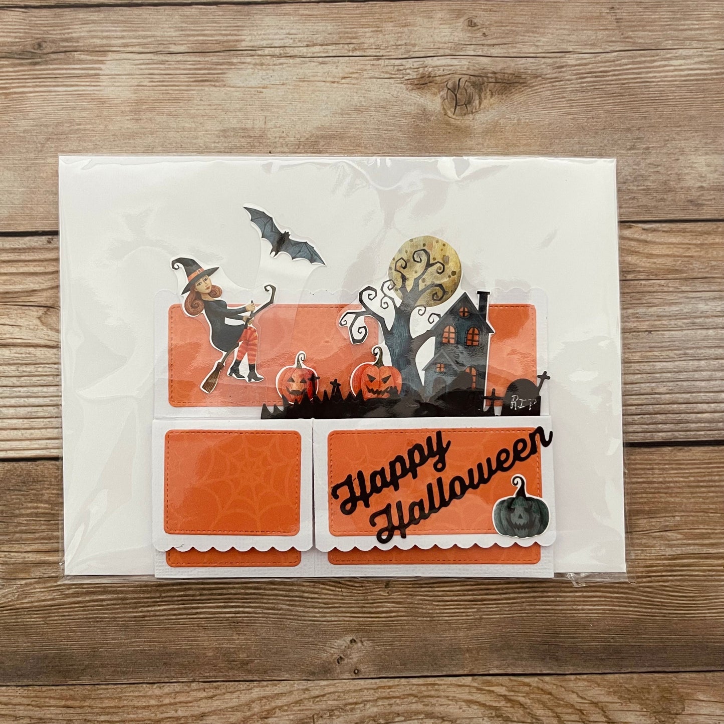 Halloween-themed card with a witch, pumpkins, and haunted house on a wooden surface