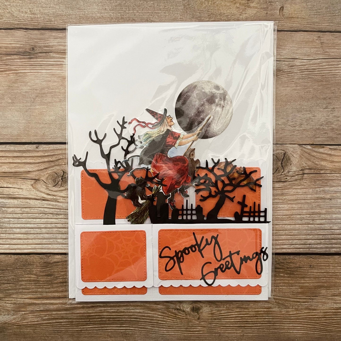 Halloween-themed card with witch and moon design on a wooden surface