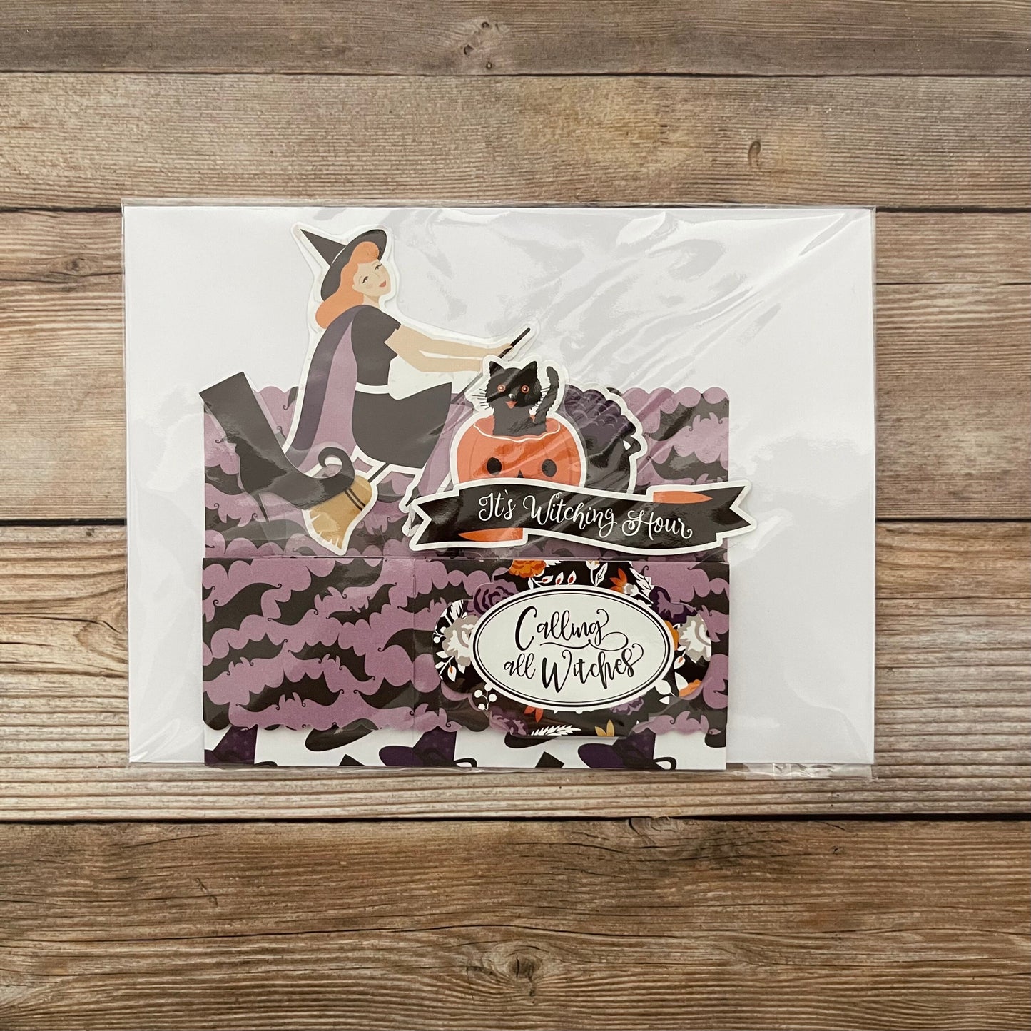 Halloween-themed card with a witch and cats on a wooden surface
