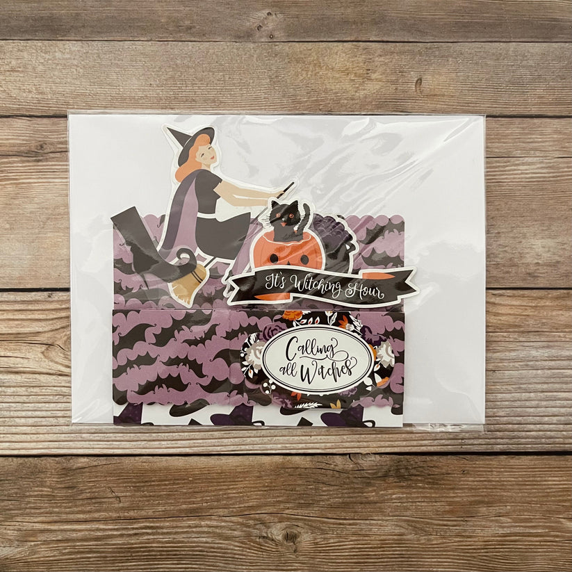 Halloween-themed card with a witch and cats on a wooden surface