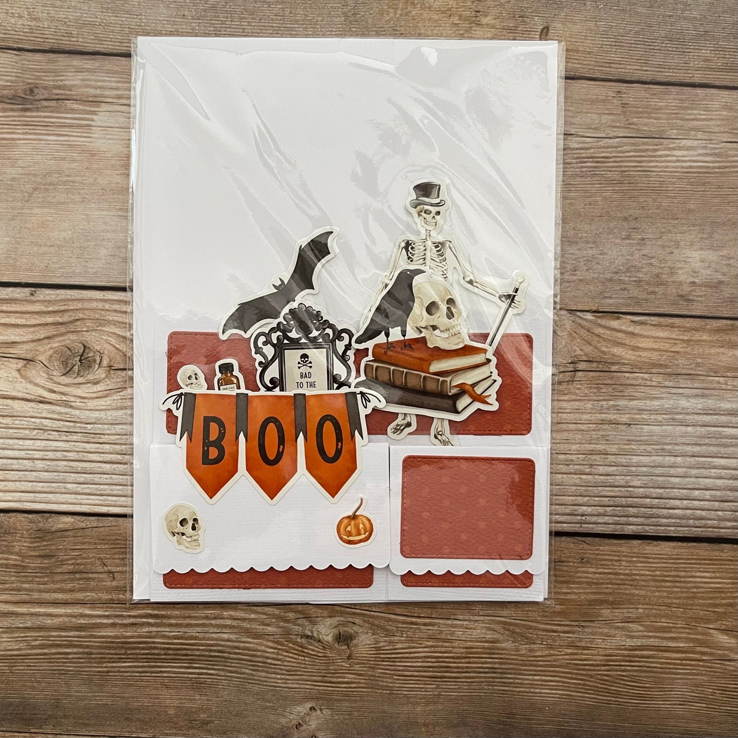 Halloween-themed card with skeleton, bat, and 'BOO' banner on a wooden surface
