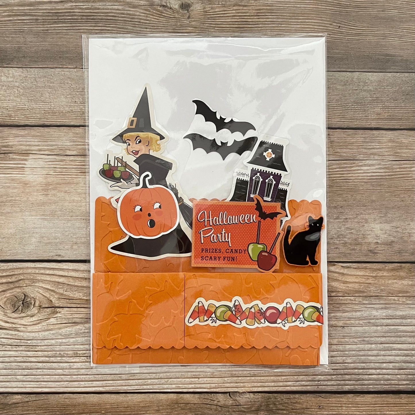 Halloween-themed card with pumpkins, witch, bats, and candy on a wooden surface