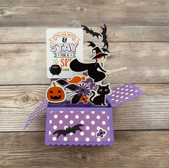 Halloween-themed pop-up card with witch, pumpkins, and cats on a wooden surface