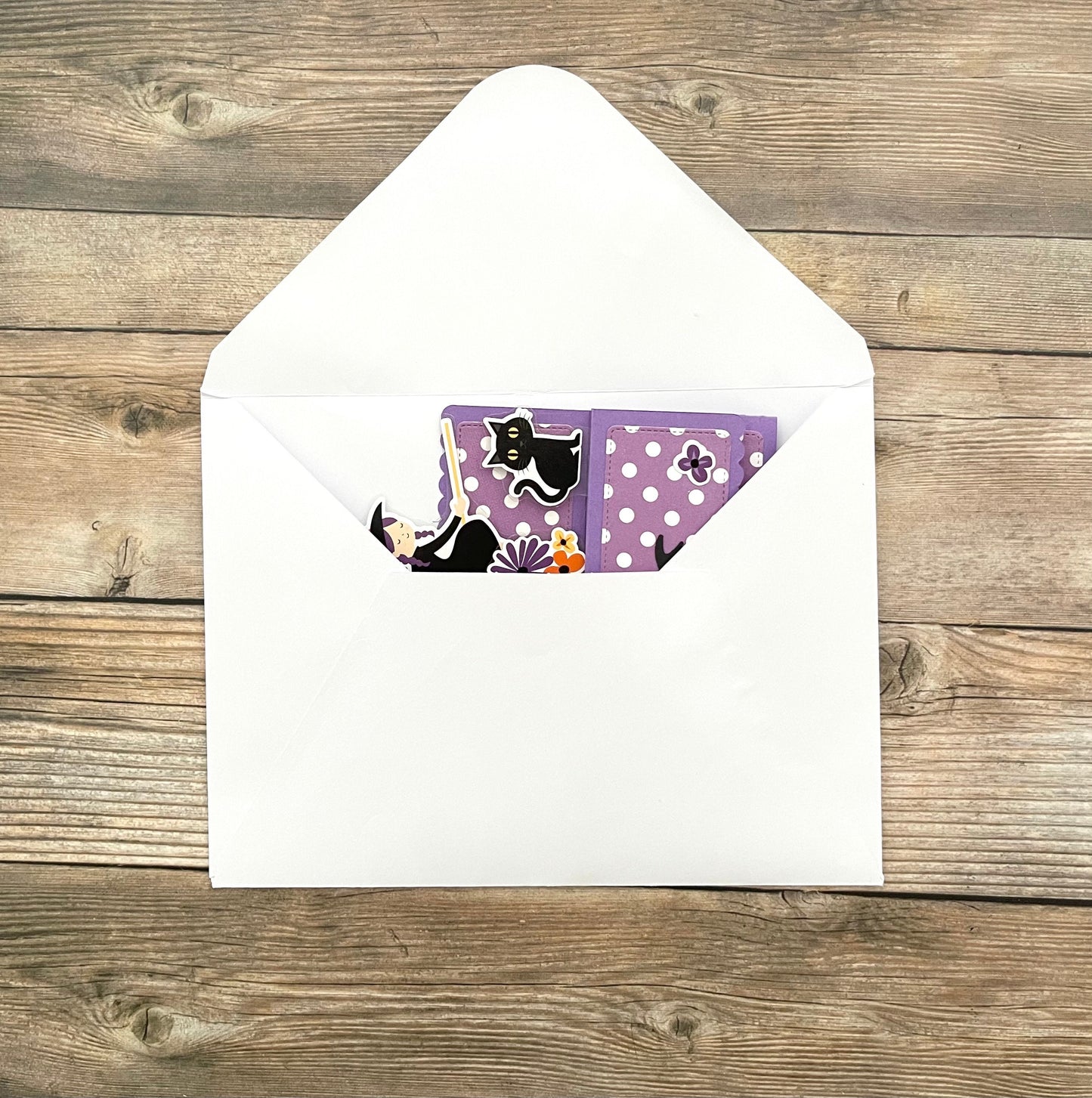 Envelopes with a purple card featuring a black cat design on a wooden surface