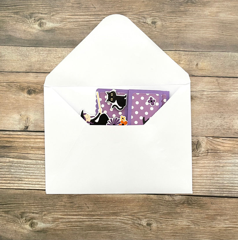 Envelopes with a purple card featuring a black cat design on a wooden surface