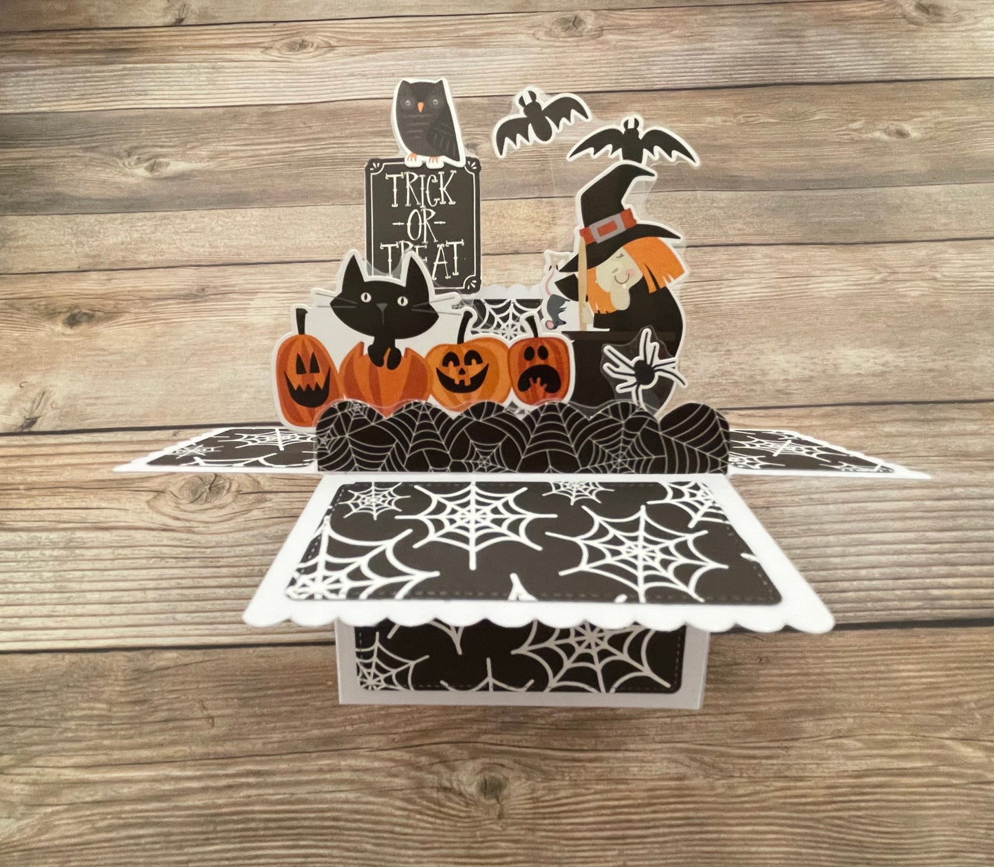Halloween-themed pop-up card with pumpkins, cats, and a witch on a wooden surface.