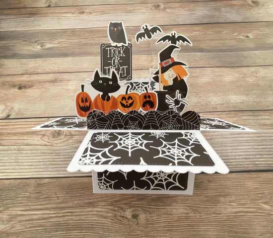 Halloween-themed pop-up card with pumpkins, cats, and a witch on a wooden surface.