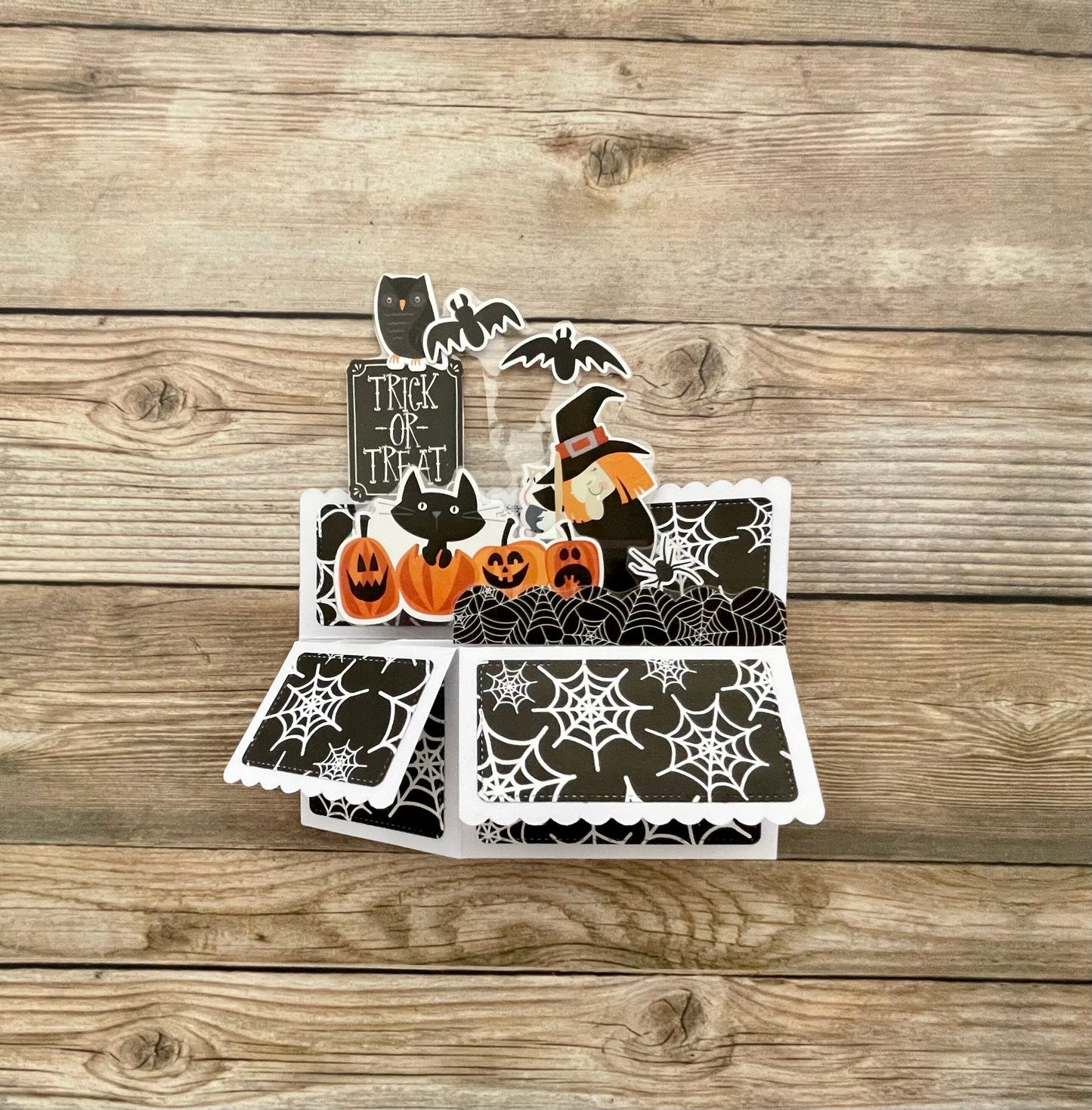 Halloween-themed card with pumpkins, cats, and bats on a wooden surface