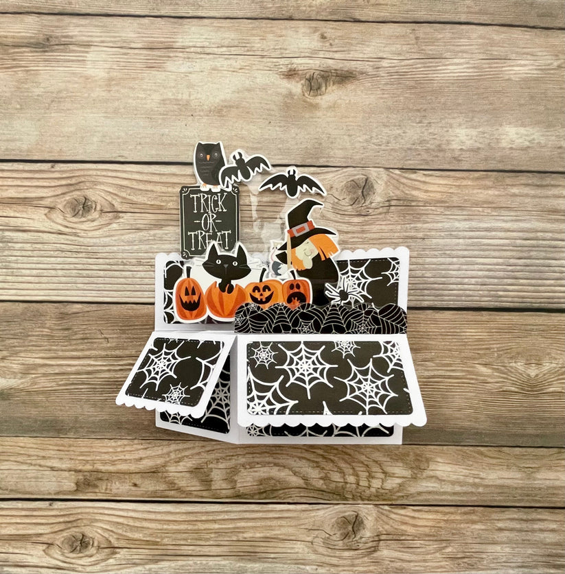 Halloween-themed card with pumpkins, cats, and bats on a wooden surface