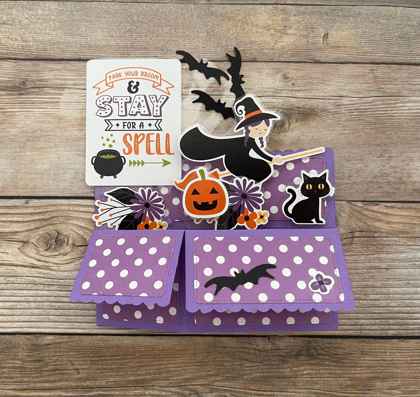 Halloween-themed pop-up card with witch, pumpkin, and bats on a wooden surface