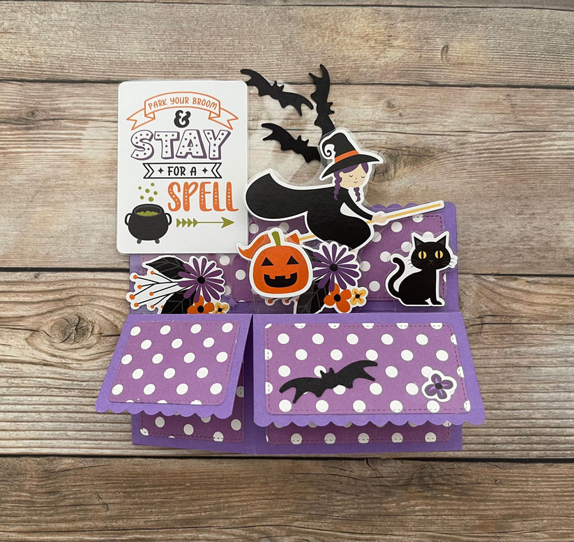 Halloween-themed pop-up card with witch, pumpkin, and bats on a wooden surface